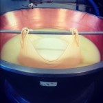 Cheese curds being strained in a large copper vat during the cheese-making process.