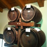 Wooden barrels stacked in a cellar for aging wine or spirits under an exposed wooden beam ceiling.
