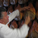 A person inspecting hanging cured hams in a storage area, ensuring quality and readiness for distribution.