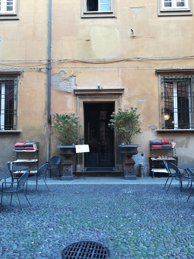 Historic Bologna courtyard with outdoor seating and rustic building façade.