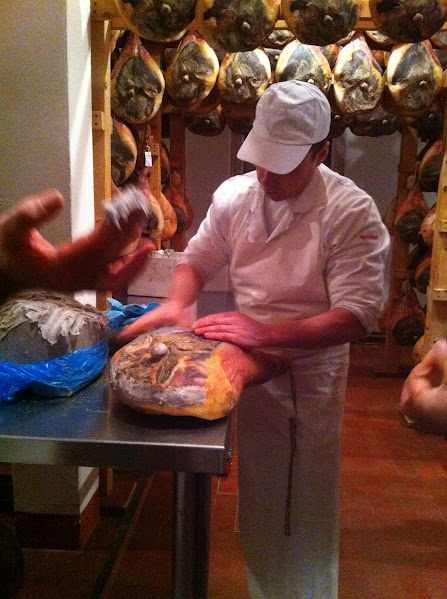 A worker prepares cured hams in a traditional drying room, showcasing artisanal meat processing techniques.
