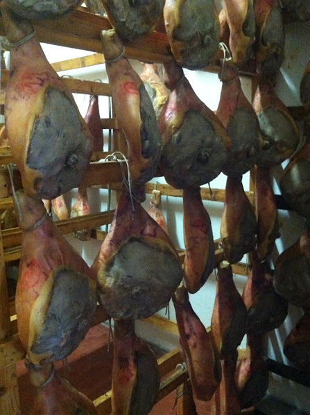 Cured ham legs hanging on wooden racks in a traditional meat drying room.