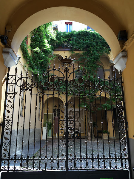 Ornate wrought iron gate with lush courtyard and ivy-draped walls in a historic European building passage.