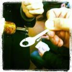 Pouring balsamic vinegar onto a plastic spoon for tasting during a culinary event with blurred background.