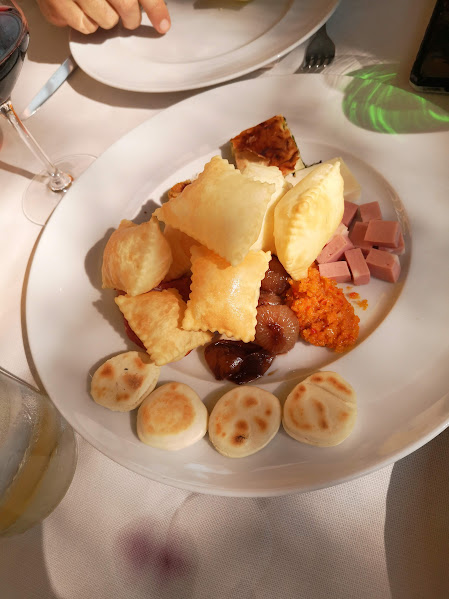 Assorted appetizers on a white plate, including fried pastries, mini torta fritta , diced ham, and chutney.