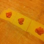 Fresh ravioli sheets with pumpkin filling placed on a wooden surface, ready for folding and cooking.
