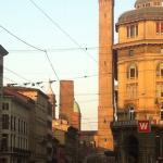Historic towers in Bologna, Italy, with bustling street scene and classic architecture under a clear sky.