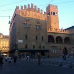 Historic Palazzo Re Enzo in Bologna's Piazza Maggiore at sunset, with people strolling nearby.