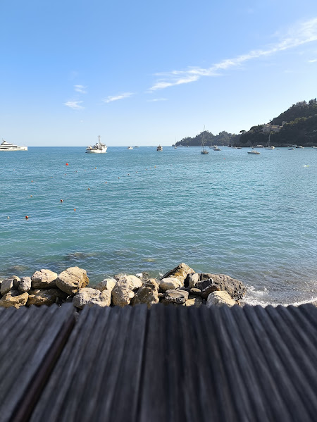 Tranquil seaside view with boats on turquoise water and rocky shoreline under a clear blue sky.