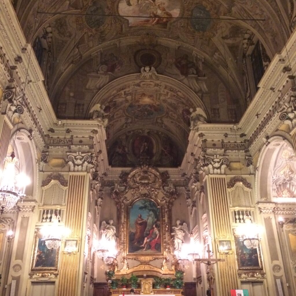 Ornate Baroque church interior with detailed frescoes, chandeliers, and religious paintings.