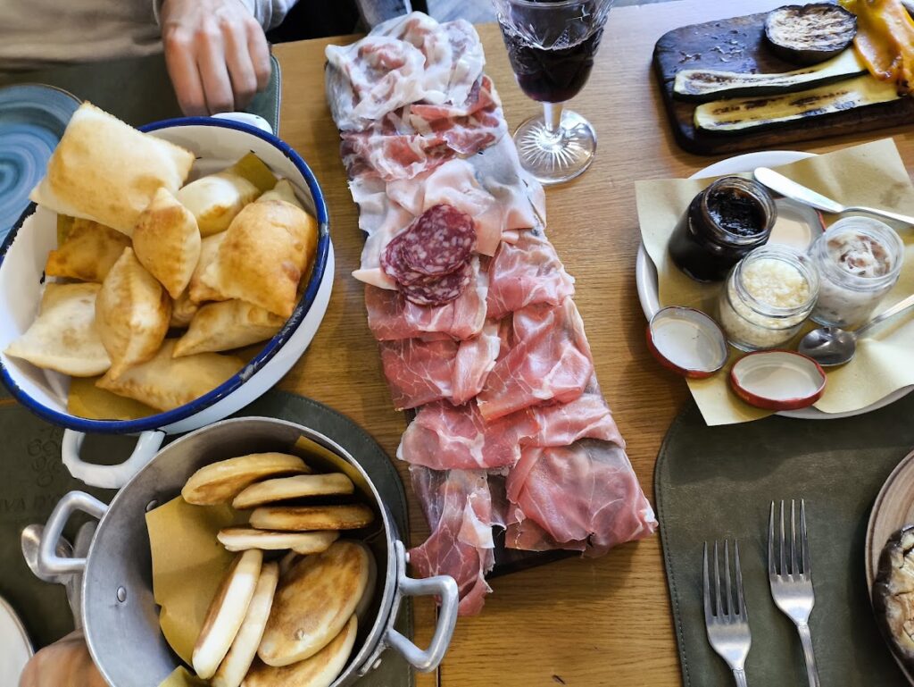 Parma charcuterie platter with cured meats, fried pastries, flatbreads, and condiments on a wooden table.