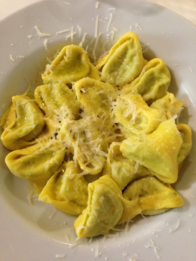 Plate of stuffed tortellini pasta with grated cheese garnish.