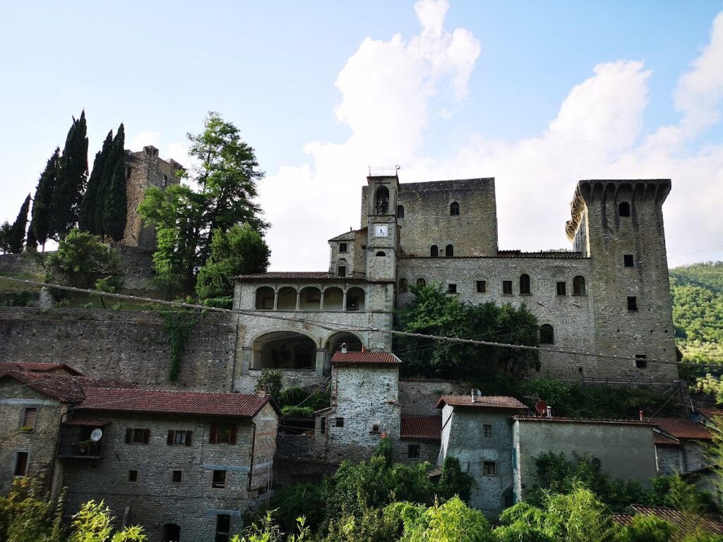 Medieval castle and stone buildings in lush Italian countryside beneath a blue sky with fluffy clouds.