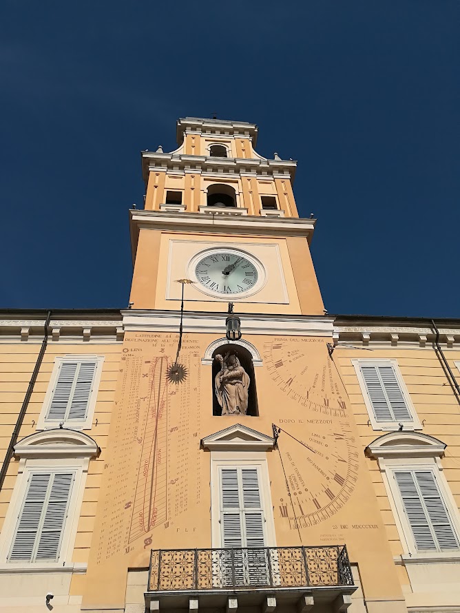 Clock tower with sundial and statue on a historic building under clear blue sky.