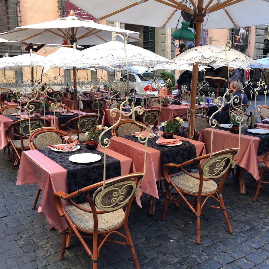 Bologna Outdoor cafe with pink tablecloths and vintage chairs under white parasols, set for dining on cobblestone street.