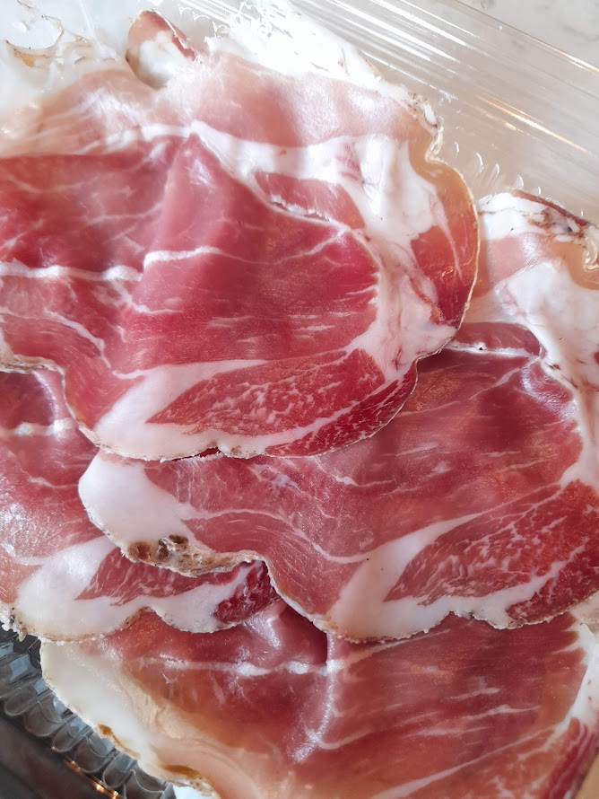 Sliced cured meat displayed in a clear plastic container, showing marbled textures.