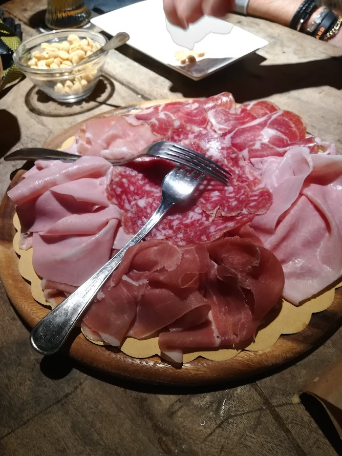 Plate of assorted cured meats with forks on a wooden table, perfect for a delicious appetizer spread.