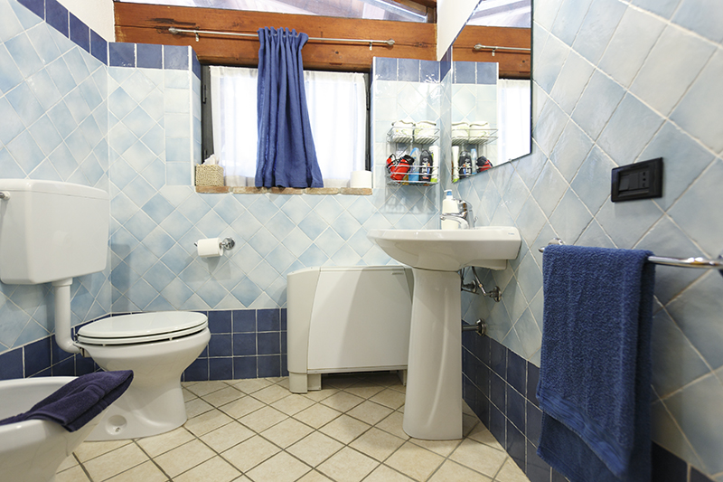 Small bathroom with blue tiles, toilet, sink, and window with blue curtains. Neat and organized interior design.