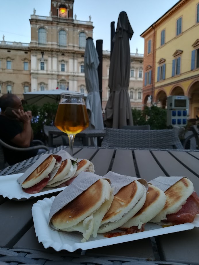 Italian piadina and beer on a table in a scenic outdoor setting with historic buildings in the background.