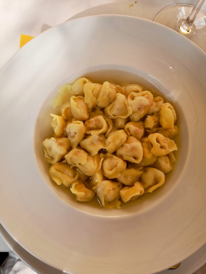 Plate of delicious tortellini in broth on a white table setting, showcasing Italian culinary delight.
