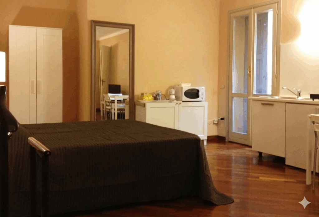 Modern bedroom with wooden floors, a bed, mirror, wardrobe, and a kitchenette with a microwave and sink.
