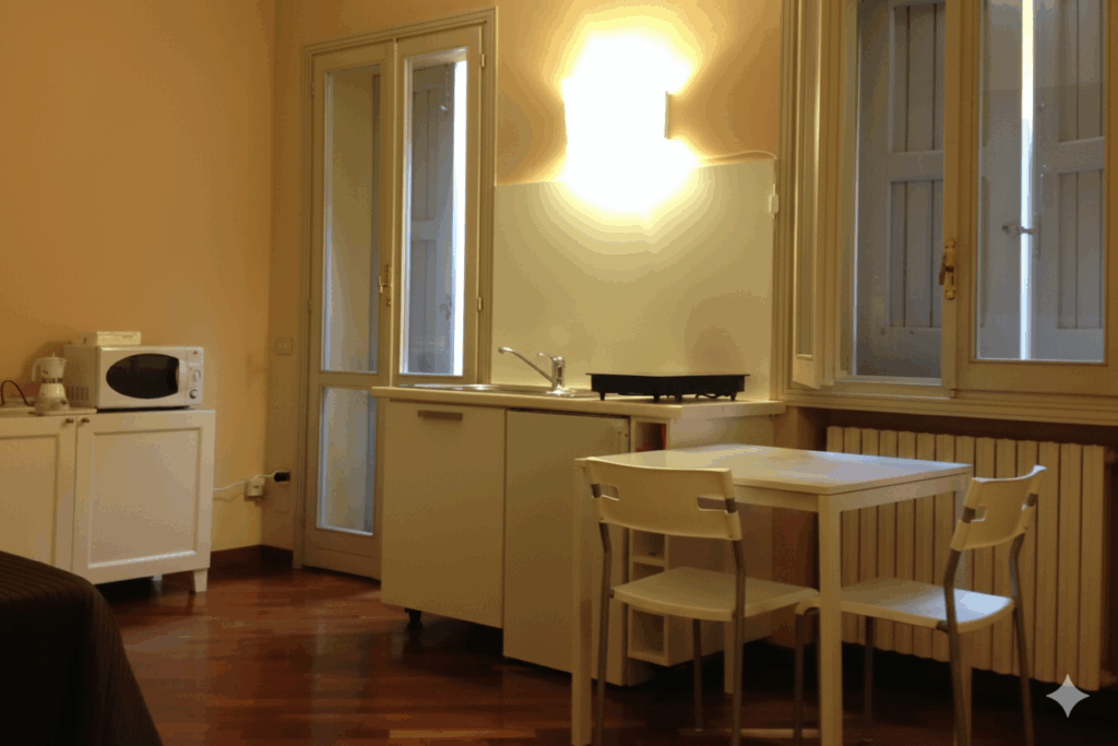 Cozy studio kitchen with wooden flooring, microwave, table, and chairs, illuminated by warm light.