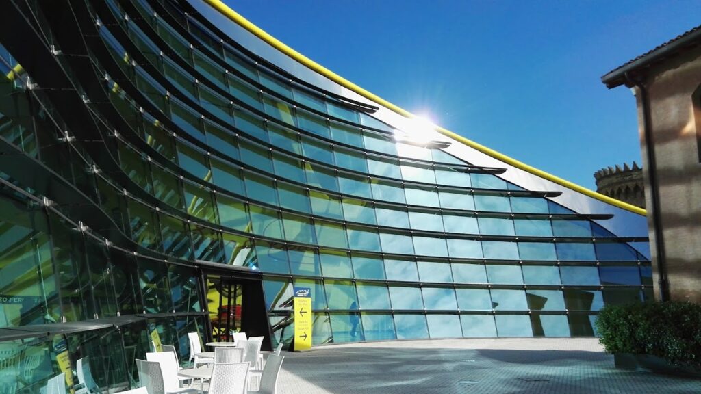 Futuristic glass building with curved facade reflecting sunlight, set against a clear blue sky. Modern architecture.
