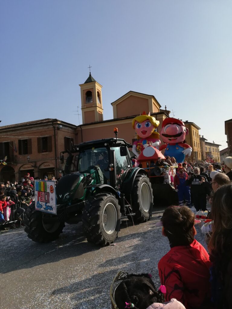 Carnival float parade passing through an Italian town piazza with church in the background