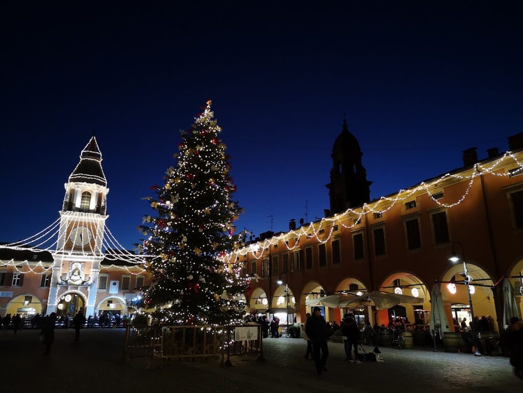 Christmas tree and festive lights in an Emilia-Romagna piazza with porticoes at dusk