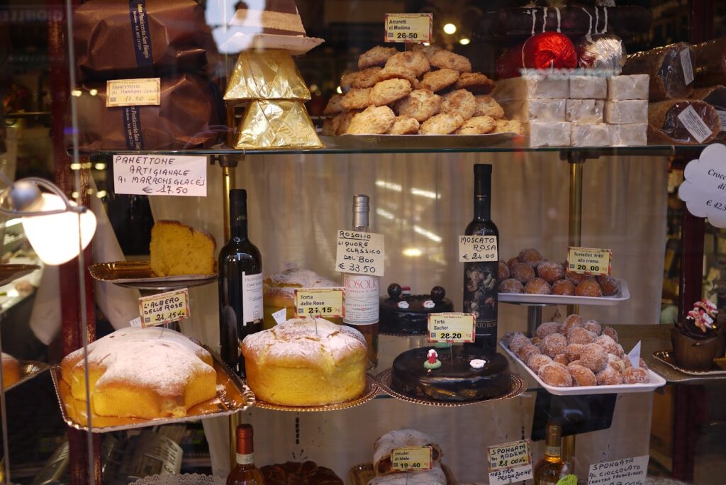 Italian bakery window displaying panettone, torta delle rose and traditional Christmas desserts with handwritten price tags